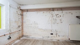 Abgeplatzte weiße Wand mit sichtbaren Leitungen und Heizkörper